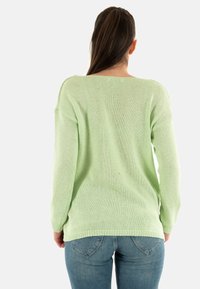 Maglione lavorato a maglia verde chiaro con una vestibilità ampia, scollatura larga e maniche lunghe. La texture è morbida, con bordi a coste e una finitura leggermente trasparente.