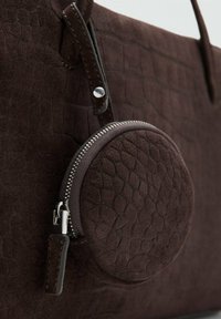 Bolso de mano de ante texturizado marrón con un monedero circular con cremallera, herrajes plateados y un acabado suave. Presenta una forma sólida y un diseño elegante.