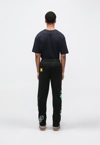 Czarne spodnie dresowe z elastycznym pasem, ozdobione żółtą gwiazdą i zielonymi akcentami. Połączone z granatowym, krótkim rękawem koszulką.