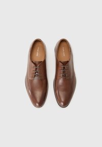 Chaussures en cuir marron avec une texture lisse, bout arrondi, et un design à lacets à six œillets. Présentent une couture discrète et une esthétique minimaliste.