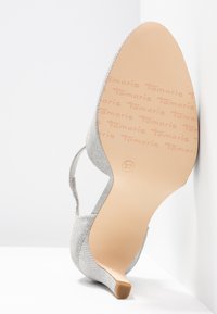 Chaussure argentée à talons hauts avec une tige en tissu texturé, bout pointu et talon aiguille. Marquage de la marque visible sur la semelle.