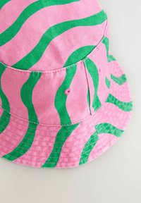 Rosa Bucket Hat mit grünen Wellenmustern, aus einem Stoff mit strukturierter Oberfläche. Verfügt über sichtbare Nähte und Belüftungslöcher.