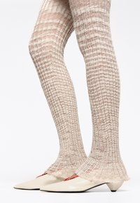 Medias de punto acanalado en color beige con un puño acampanado. Combinadas con tacones color crema de punta afilada con un sutil acento rojo en el costado.