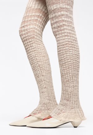 Medias de punto acanalado en color beige con un puño acampanado. Combinadas con tacones color crema de punta afilada con un sutil acento rojo en el costado.