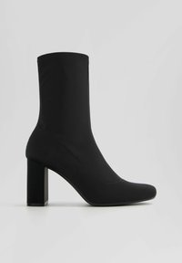 Bottine noire à tige en tissu lisse, bout pointu et talon carré. Dotée d'une silhouette élégante et de coutures minimales.