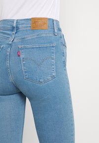 Jeans de color azul claro con un diseño ajustado, que presentan dos bolsillos traseros y un parche de marca de cuero en la cinturilla con detalles en relieve.