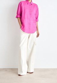 Rosa linnen skjorta med knappar och uppvikta ärmar, kombinerad med vita vida cargo-byxor som har sidofickor och veck. Bruna sandaler.