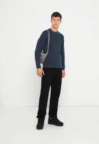 Tumes ribakudum mantel, mustad püksid ja mustad kingad. Mudel kannab väikest halli õlakotit pika rihmaga. Minimalistlik disain.