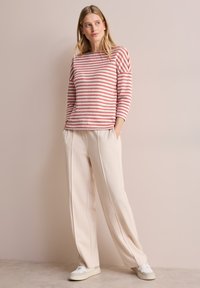 Suéter a rayas en rosa y blanco, con mangas tres cuartos. Pantalones de pierna ancha en color crema con costuras frontales y tenis blancos.