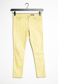 Jeans amarillos slim-fit con botón y cremallera, bolsillos frontales, colgados en una percha negra sobre un fondo blanco.