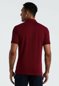 Burgunderfarbenes Poloshirt mit kurzen Ärmeln, kontrastierendem marineblauen Kragen und Ärmelsäumen, aus glattem, atmungsaktivem Stoff; figurbetonter Schnitt.