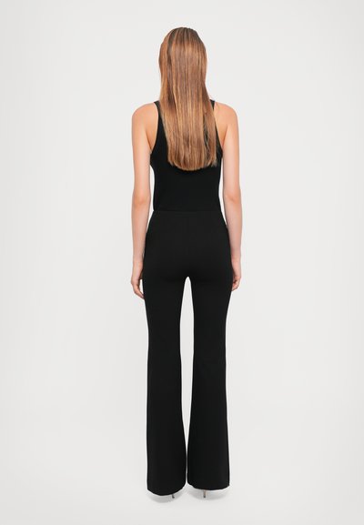 Black jumpsuit with a fitted top and flared legs, featuring a smooth texture and sleeveless design, viewed from the back.