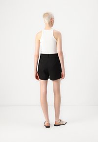 Svarta shorts med en skräddarsydd design och mjukt tyg, i kombination med en vit tanktop. Personen ses från ryggen, med kort hår.