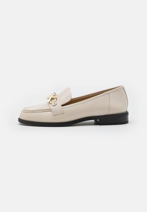 Mocassin en cuir beige avec semelle noire et boucle décorative en métal doré sur fond blanc uni, vue de profil.
