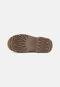 Suola in gomma marrone con un pattern zigzag testurizzato e caratteristiche di grip circolare, progettata per trazione e durata.