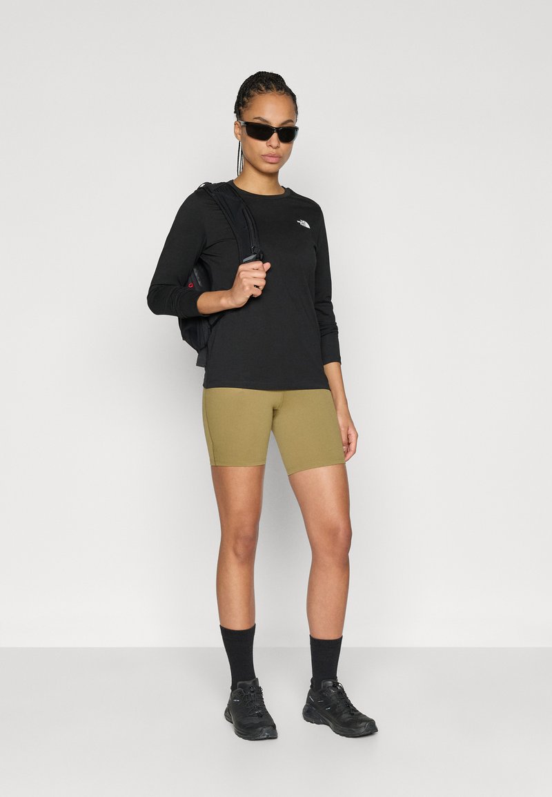 Svart långärmad tröja, olivgröna shorts, svart ryggsäck, solglasögon, svarta strumpor och svarta träningsskor. Enkel och funktionell design.