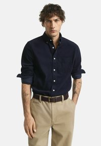 Mariene button-up shirt, zachte textuur, lange mouwen, omgeslagen bij de mouwen, met borstzak. Beige chinos en een bruine leren riem maken de outfit compleet.