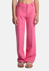 Pantaloni a palazzo rosa con una texture liscia, caratterizzati da una chiusura a bottone e una vestibilità sartoriale. Indossati con sandali argentati.