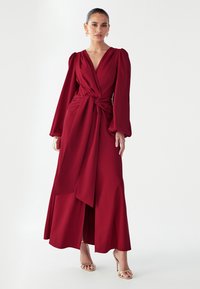 Pikk burgundia punane kleit sügava V-kaelusega, pikendatud varrukatega, drapeeritud vöökohaga ja külje läbilõikega. Sile kangas voolava, elegantse disainiga.