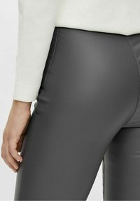 Graue Leggings aus Kunstleder mit glatter Textur, figurbetonten Design und sichtbaren Nähdetails, getragen mit einem hellen Pullover.