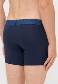Tengerészkék boxer alsó, puha anyagból, textúrált kék derékrésszel, szűk illeszkedéssel és minimális varrási részletekkel.