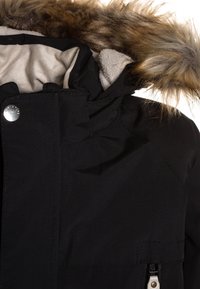 Veste d’hiver noire avec capuche bordée de fourrure, doublure intérieure beige, bouton-pression et détail de poche zippée.