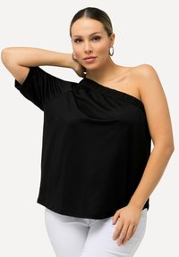 Sort off-shoulder top med en afslappet pasform, rynket halsudskæring, korte ærmer og glat tekstur, parret med hvide bukser.