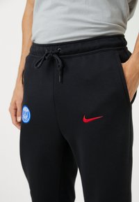Sorte sweatpants med snørelomme, udstyret med et blåt Paris Saint-Germain-logo og en rød Nike swoosh. Blødt stof med sidelommer.
