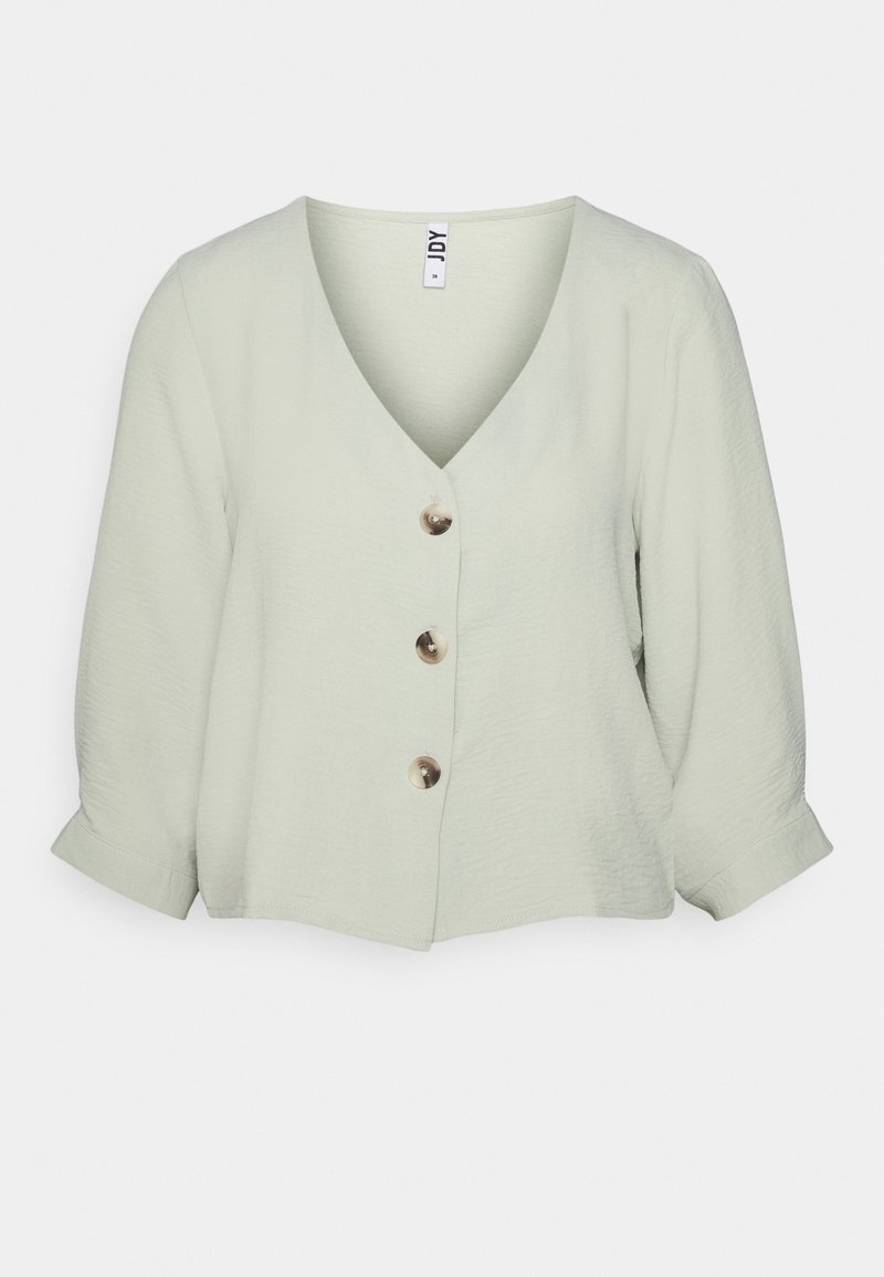 Blouse courte vert clair texturée avec un col en V et trois gros boutons sur le devant. Manches trois-quarts avec revers roulés.