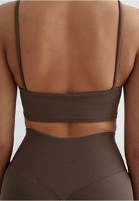 Bruine sporttop met korte mouwen en dunne bandjes, gemaakt van een gladde stof. Opvallend logo aan de achterkant, gecombineerd met hoge taille bijpassende onderkleding.