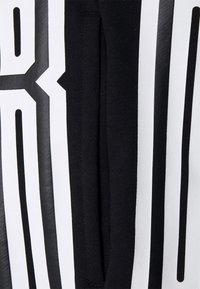 Gros plan d’un tissu en maille noire avec un grand imprimé géométrique blanc et noir comprenant des lignes verticales et diagonales audacieuses.