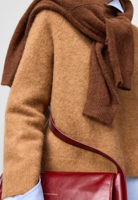 Pull en laine marron clair avec un col côtelé, superposé avec une écharpe marron foncé. Un sac à main en cuir rouge est porté sur l'épaule.