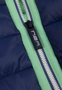 Marineblaue isolierte Jacke mit einem grünen Reißverschlussband und kontrastierenden weißen Zähnen. Ein schwarzer Ziehgriff trägt das Logo „n2a.“
