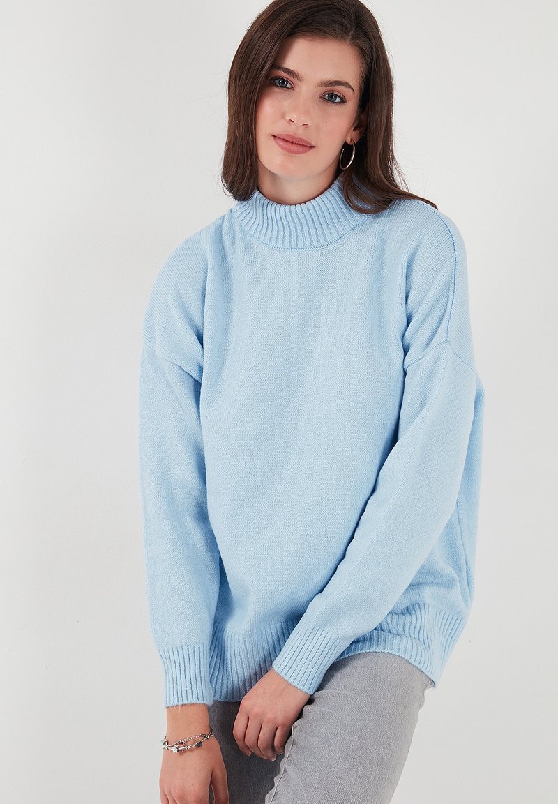 Gaiši zilas adītas džemperis ar augstu apkakli, garām piedurknēm un ribotām aprocēm. Mīksta tekstūra un brīva piegriezuma, piemērots ikdienas valkāšanai.