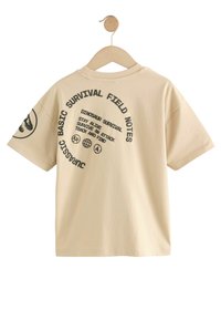 Beige bomulds t-shirt med korte ærmer, har sorte grafiske tekster og symboler på ryggen, rund halsudskæring og en afslappet pasform.