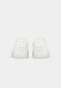 White sneakers with embossed circular patterns, smooth texture, and padded collar. Features brand logo at the back and a flat sole.