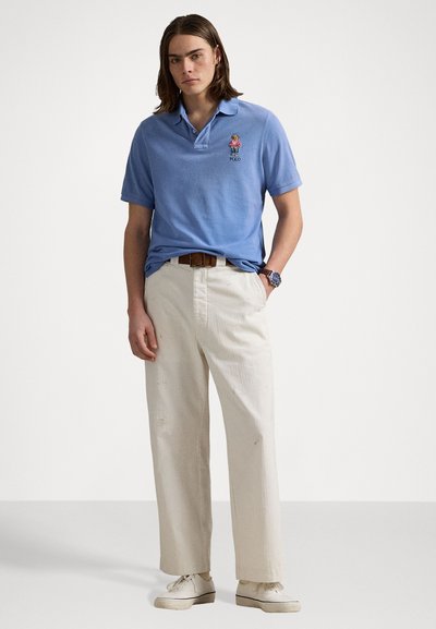 Light blue polo shirt with a collar and a small embroidered logo. Paired with relaxed-fit white trousers and white sneakers.