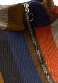 Chiusura lampo in metallo con anello su tessuto a strisce multicolore nei toni di blu, marrone, arancione e grigio.