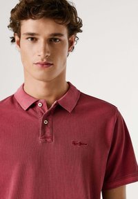 Camisa tipo polo roja de algodón con un acabado texturizado. Cuenta con una tapeta de dos botones, logo bordado en el pecho y mangas cortas.