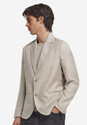 Ljusbeige kavaj med notched krage, två knappar och sidofickor. Tillverkad av mjukt texturerat tyg, skräddarsydd passform och minimala detaljer.