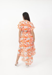 Blumen-Maxikleid in Orange, mit kurzen Rüschensäumen, einer taillierten Taille und einem geschichteten Saum. Leichter, fließender Stoff mit bunten Blumen.