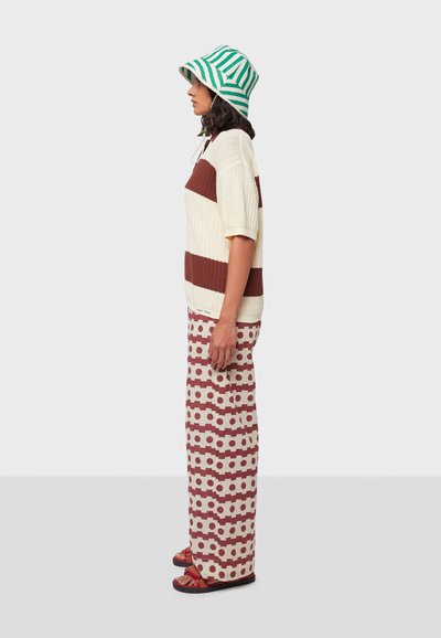 Gehaakte gestreepte trui in romig wit en bruin, gecombineerd met gebloemde wijde broek in rood en beige. Aangevuld met een groene gestreepte emmerhoed.