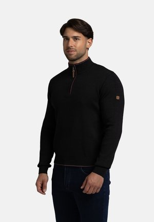 Suéter negro con cremallera en el cuello hecho de tela de punto. Presenta una cremallera burdeos en contraste y una insignia texturizada en la manga izquierda.