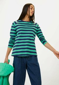 Langsleeve gestreepte blouse in groen en marineblauw met een ronde halslijn. Zachte stof met een losse pasvorm, gecombineerd met hoge taille blauwe jeans.