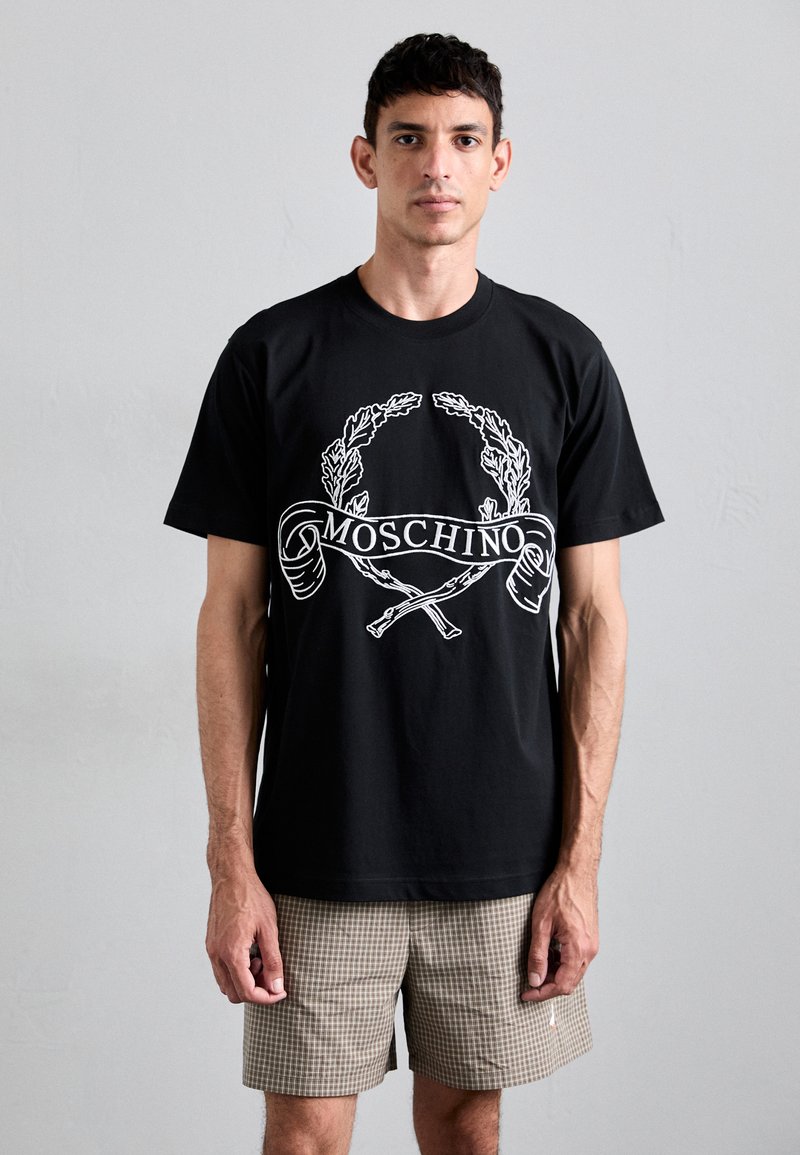 Μαύρο μπλουζάκι από βαμβάκι με λευκή εκτύπωση γραφικών με φύλλα δάφνης και κείμενο "MOSCHINO". Μοντέλο με καρό σορτς.