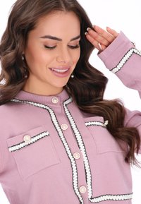 Rózsaszín kardigán fekete és fehér díszítéssel, gyöngygombokkal és két elülső zsebbel. Puha tapintású és fitted kialakítású.