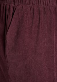 Burgundy corduroy fabric with vertical ribs, featuring an elastic waistband and side pocket detail. Soft texture.