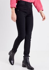 Jeans skinny noirs avec une taille haute, texture lisse et coutures latérales discrètes, associés à des bottines noires élégantes.