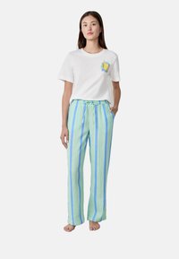 T-shirt bianca in cotone con grafica di limone e maniche corte azzurro chiaro, abbinata a pantaloni con cordino a righe verde chiaro e blu.