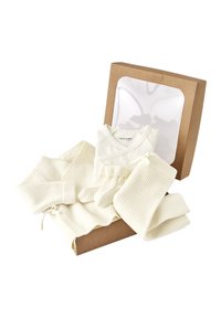 Cremefarbene, gerippte Babykleidung bestehend aus Sweater, Hose, Socken und einem Wickeloberteil, neben einem braunen Geschenkkarton mit einer klaren Fensterfront präsentiert.